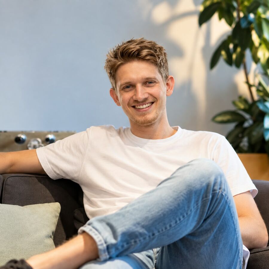 Porträt von Philipp Paulik, lächelnd auf einem Sofa vor einer Pflanze